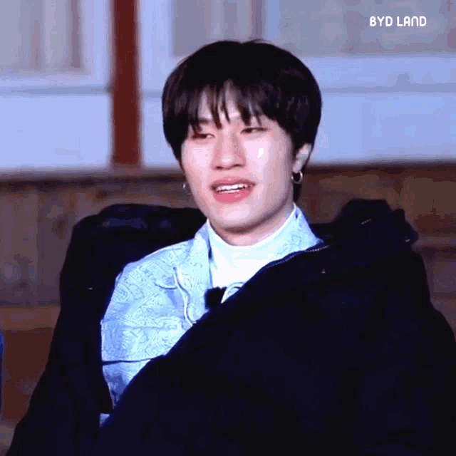 a young man wearing a blue shirt and a black jacket with the words byd land on the bottom right