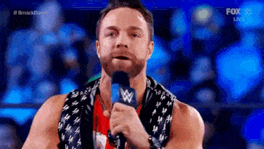 a wrestler is speaking into a microphone while wearing a scarf with the letter w on it .