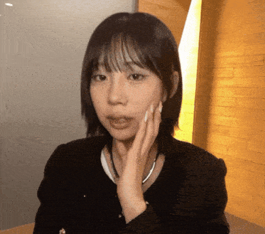 a woman in a black jacket has her hand on her face