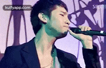a man is singing into a microphone while wearing a black jacket .