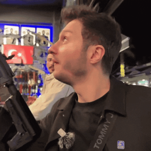 a man wearing a black tommy j jacket holds a rifle
