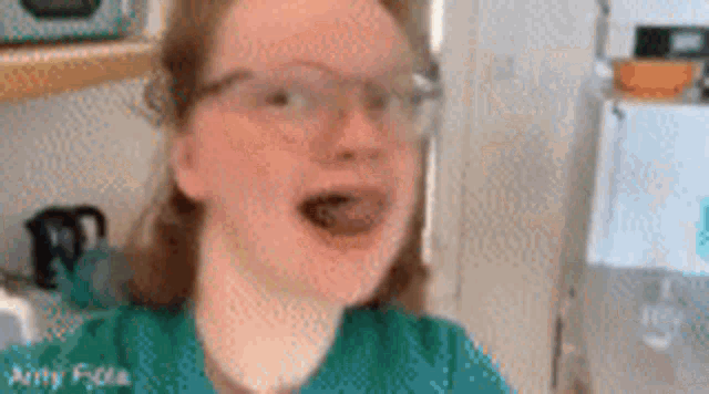 a girl wearing glasses is making a funny face in a kitchen .