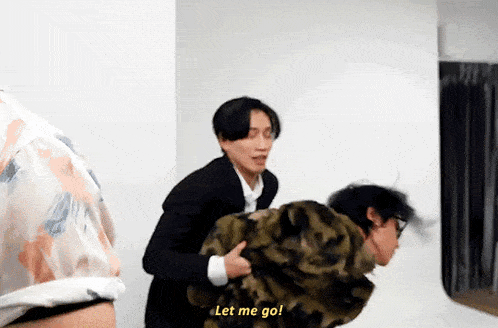 a man in a suit holds another man in a camouflage jacket and says " let me go "