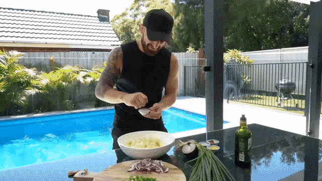 a man prepares food in front of a pool with a bottle of olive oil on the table