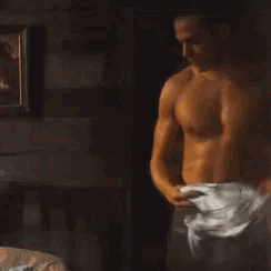 a shirtless man is taking off his shirt in a dark room