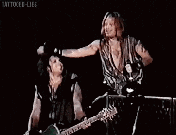 two men are standing next to each other on a stage while one of them is playing a guitar .
