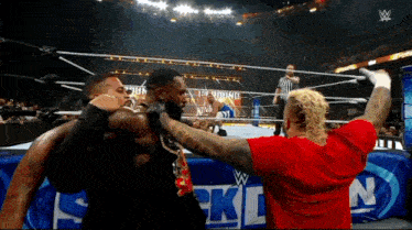 a man in a red shirt stands in a wrestling ring