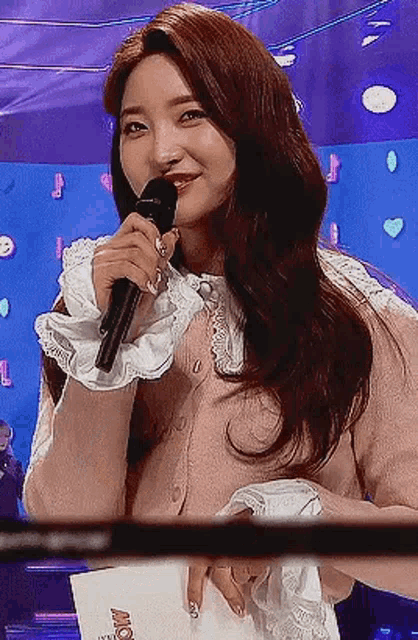 a woman is holding a microphone in her hand and smiling while standing in front of a blue background .