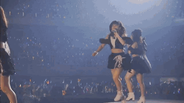 two women are singing into microphones on a stage in front of a crowd of people .