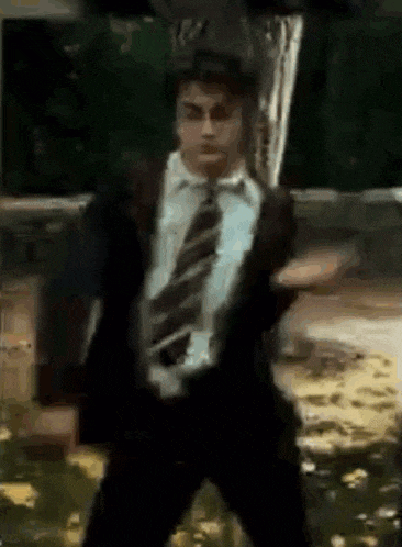 a man in a suit and tie is dancing in front of a green board .