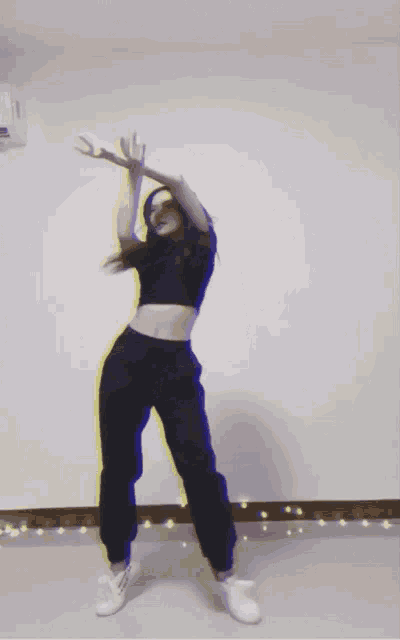 a woman is dancing with her arms outstretched in front of a wall