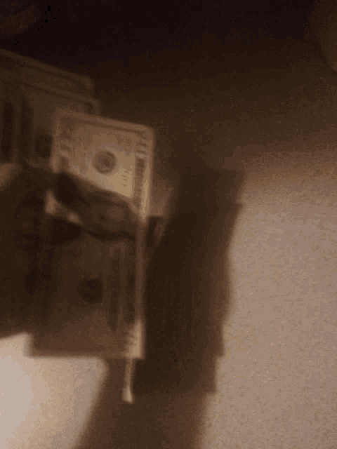 a shadow of a person holding a stack of 100 dollar bills in their hand
