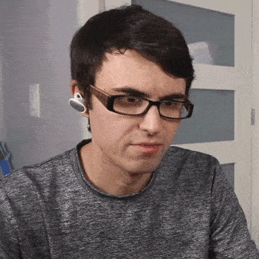a man wearing glasses and ear buds looks to his left