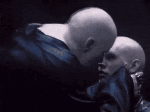 a couple of bald men are hugging each other in the dark
