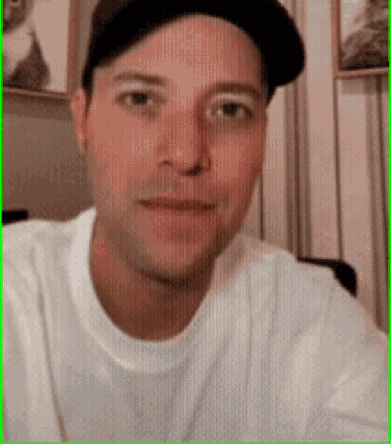 a man wearing a hat and a white shirt is looking at the camera
