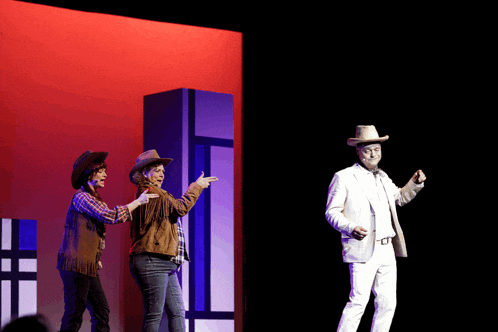 a man in a white suit and a woman in cowboy hats are on a stage