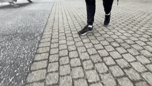 a person walking on a cobblestone sidewalk with a skateboard in the background