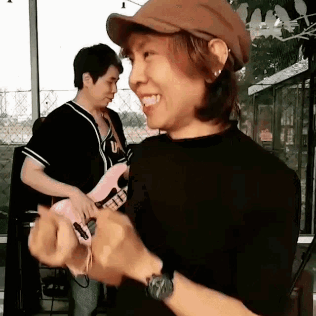 a woman wearing a hat is smiling while a man plays a pink guitar in the background .