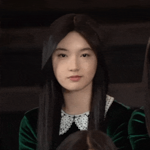 a girl with long black hair and a white collar holds her hand to her face