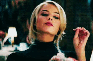 a woman in a black turtleneck is holding a pink flower in her hand and looking at the camera .