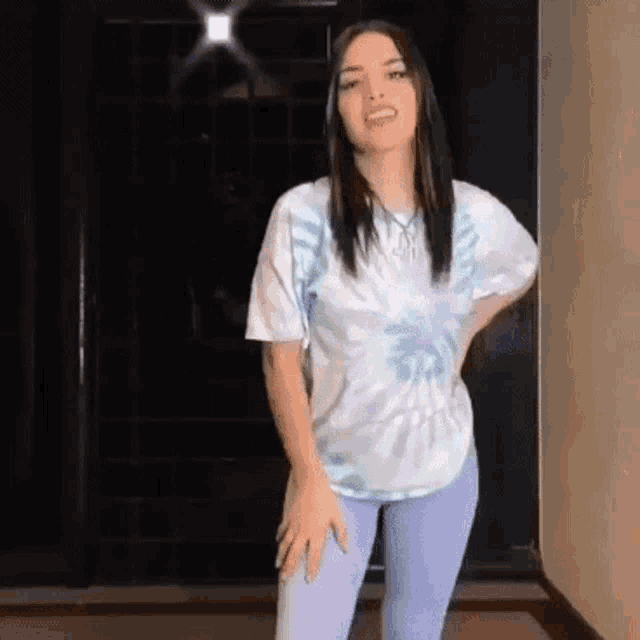 a woman wearing a tie dye shirt and purple pants is dancing in a room .