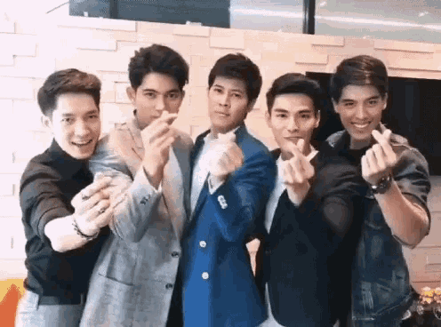 a group of young men are posing for a picture with their hands in the shape of hearts .