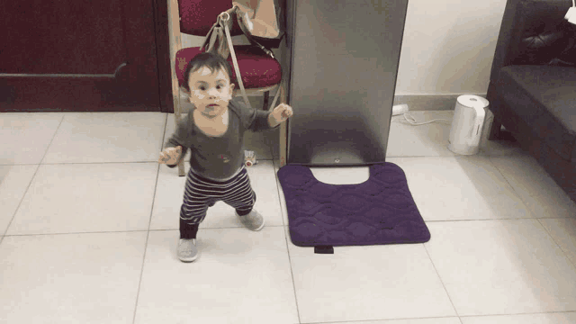 a baby standing next to a purple mat