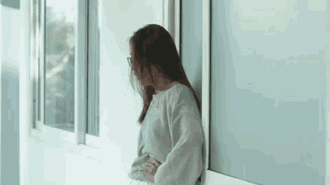 a woman is leaning against a wall and looking out of a window .