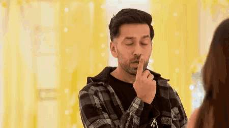 a man in a plaid shirt holds his finger to his mouth
