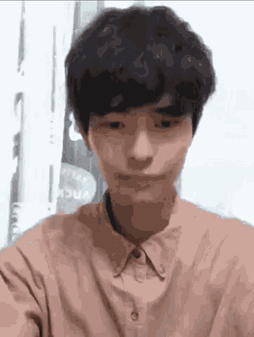 a young man in a brown shirt is making a funny face while looking at the camera .
