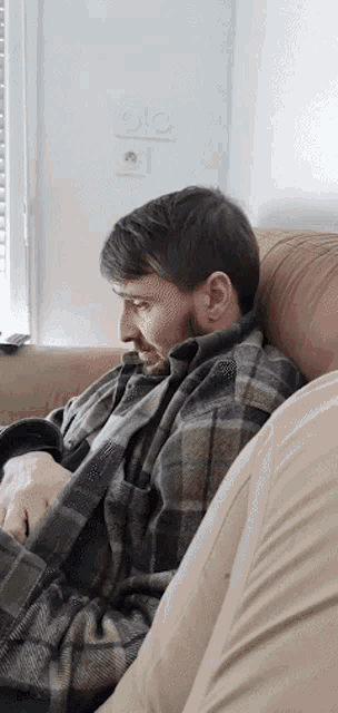 a man is sitting on a couch with a plaid blanket around his shoulders
