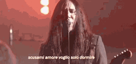 a man with long hair singing into a microphone and playing a guitar .