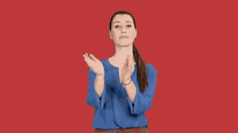 a woman in a blue shirt is clapping her hands in front of a red background