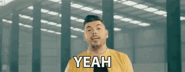 a man in a yellow shirt is standing in front of a building and saying yeah .