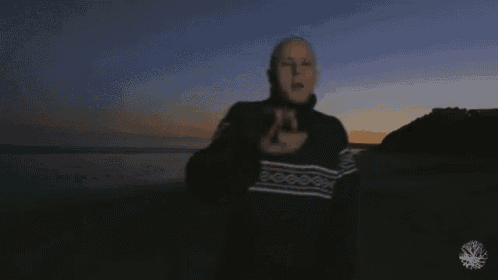a man in a black sweater is standing on a beach at sunset