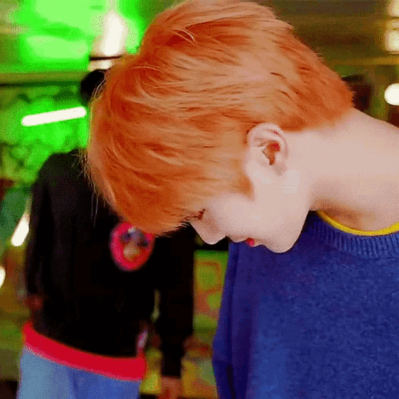 a man with orange hair is wearing a blue sweater and looking down