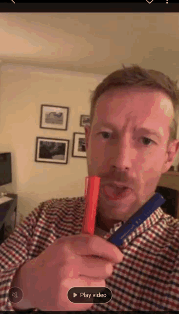 a man in a plaid shirt is holding a red stick in his mouth and the play video button is visible in the corner
