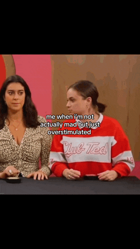 two women are sitting at a table and one of them is wearing a red and white sweater that says club ted .