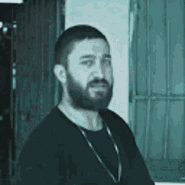 a man with a beard is wearing a black shirt and a chain around his neck .