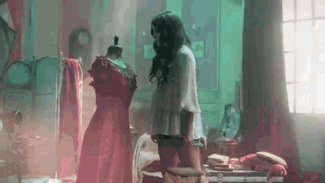a woman is standing next to a mannequin in a room looking at a red dress .