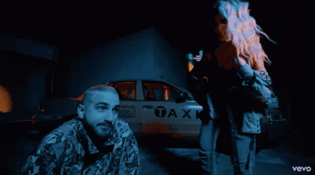 a man and woman are standing in front of a taxi that says taxi