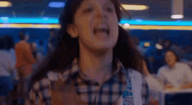 a young girl is screaming in a bowling alley while people are sitting at tables in the background .