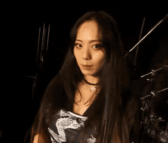 a woman with long dark hair is standing in front of a drum set .