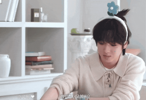 a young man wearing a headband with a flower on it is sitting in front of a bookshelf