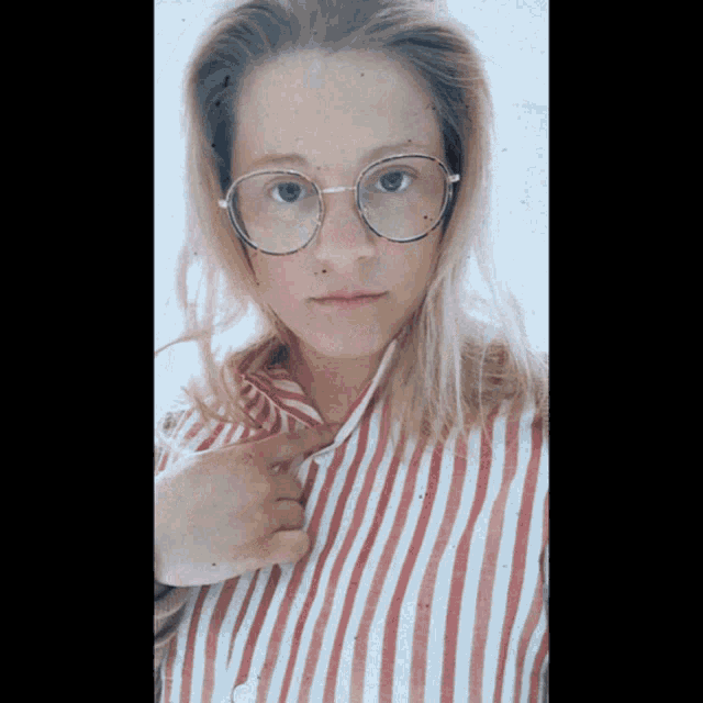 a woman wearing glasses and a red and white striped shirt looks at the camera