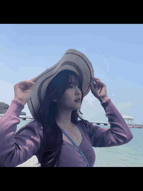 a woman wearing a purple sweater and a hat is standing in front of the ocean