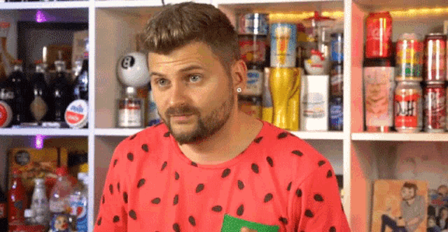 a man wearing a red shirt with black polka dots is standing in front of a shelf full of soda cans and bottles