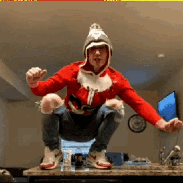 a man squatting on a counter wearing a santa hat and a red sweater