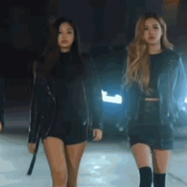 two women are standing next to each other on a street at night .