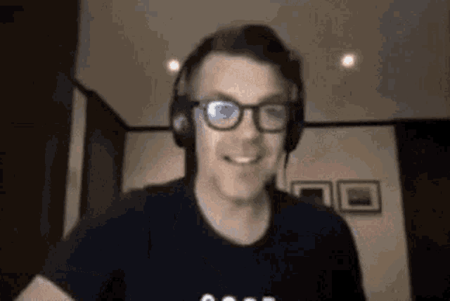 a man wearing glasses and headphones is smiling while sitting in a room .
